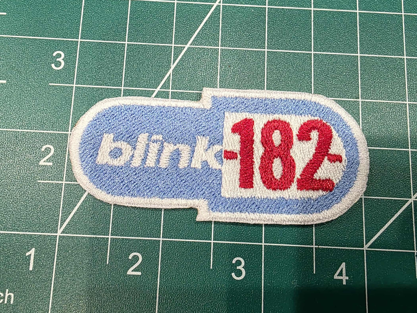 Patch with 'blink-182' logo on a green cutting mat with measurements.